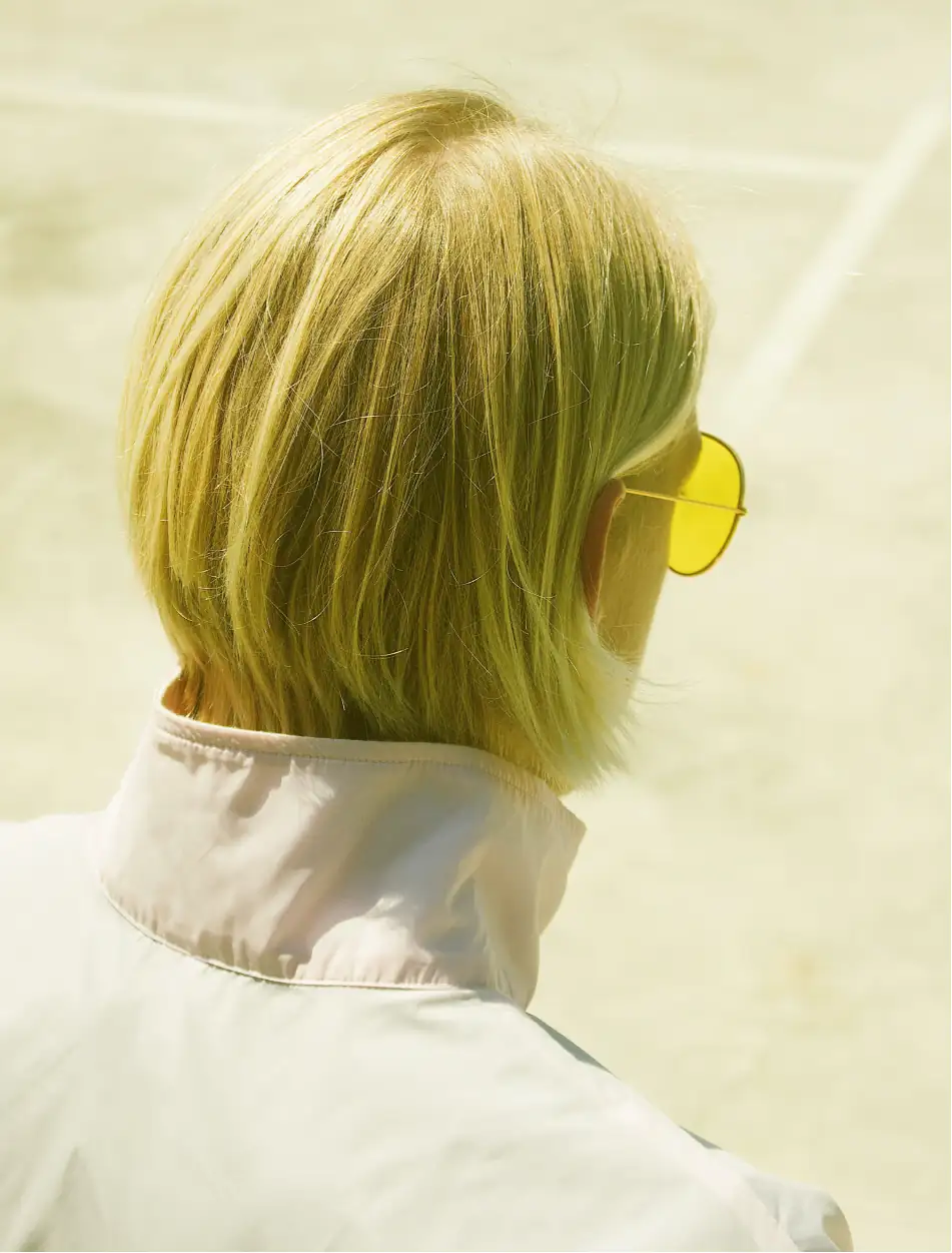 Portrait from the back of a man with yellow hair and pink sunglasses, super retro vibe